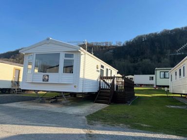 a static caravan situated on grass with a mountain backdrop at Clarach Bay Holiday Village - Holiday Accommodation 21674, Aberystwyth