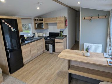 a kitchen area with a fridge, stove, and wooden cabinets at Brynowen Holiday Park - Holiday Accommodation 21677, Borth, Aberystwyth