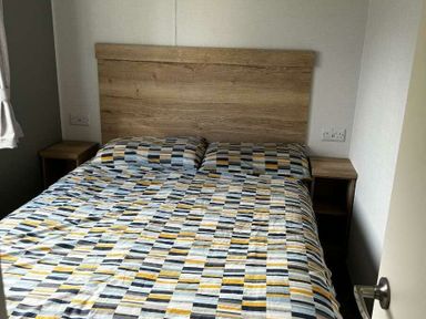 a bedroom with a wooden headboard and patterned bedding at Brynowen Holiday Park - Holiday Accommodation 21677 Borth, Aberystwyth