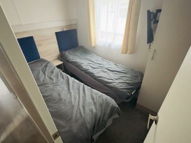 a bedroom with two single beds covered with gray bedding at Lido Beach Holiday Park - Holiday Accommodation 21682, Prestatyn