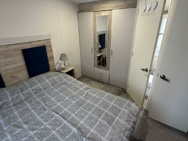 a bedroom with a bed, wardrobe, and a lamp at Lido Beach Holiday Park - Holiday Accommodation 21682 in Prestatyn