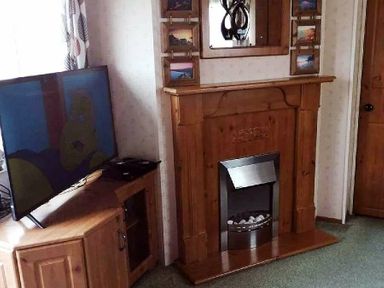 a living room with a wooden fireplace and a TV on a stand at Hafan y Mor Haven - Holiday Accommodation 21715 in Pwllheli