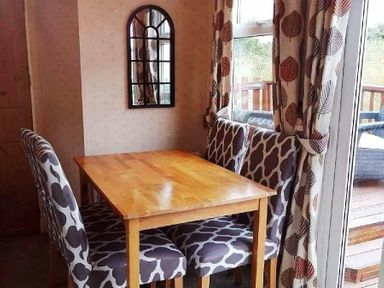 a dining area with a wooden table and patterned chairs at Hafan y Mor Haven - Holiday Accommodation 21715 Pwllheli