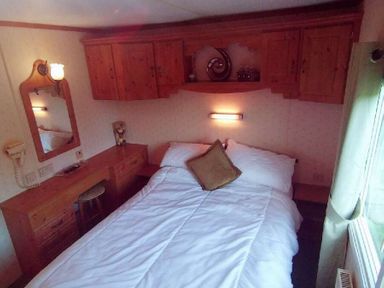 a bedroom featuring a bed, wooden cabinets, a mirror, and a desk at Hafan y Mor Haven - Holiday Accommodation 21715, Pwllheli