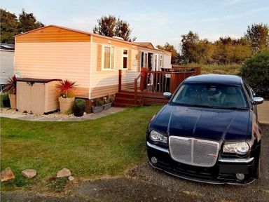 a mobile home with a deck and a black car parked beside it at Hafan y Mor Haven - Holiday Accommodation 21715 Pwllheli