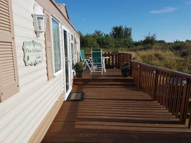 a wooden deck with green chairs and planters at Hafan y Mor Haven - Holiday Accommodation 21715 Pwllheli