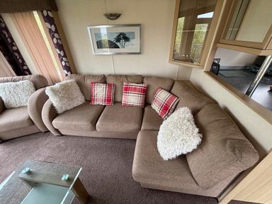 a beige sectional sofa with red plaid cushions and white throw pillows at Clarach Bay Holiday Village - Holiday Accommodation 21850, Aberystwyth