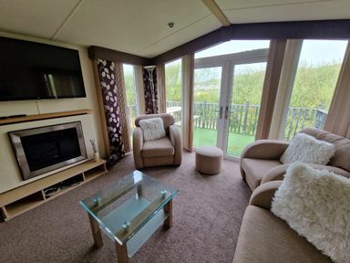 a living room with a television, sofa, armchair, coffee table, and patio doors at Clarach Bay Holiday Village - Holiday Accommodation 21850, Aberystwyth