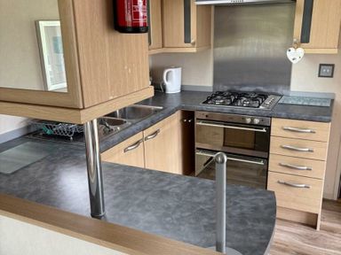 a kitchen with wooden cabinets and stainless steel appliances at Clarach Bay Holiday Village - Holiday Accommodation 21850, Aberystwyth