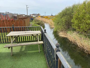 a picnic table near a small waterway with grass and bushes at Clarach Bay Holiday Village - Holiday Accommodation 21850 Aberystwyth