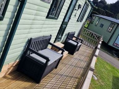 two black benches on a wooden deck outside a green building at Woodlands Holiday Park - Holiday Accommodation 21859 in Twywn