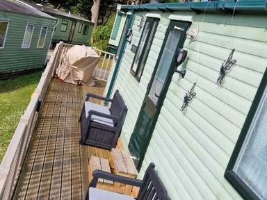 exterior view of a row of green cabins with wooden decking and outdoor seating at Woodlands Holiday Park - Holiday Accommodation 21859 Twywn