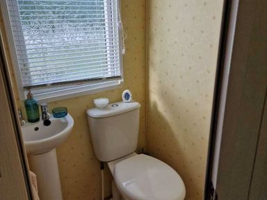 a bathroom with a toilet and basin, windows with blinds at Woodlands Holiday Park - Holiday Accommodation 21859, Twywn