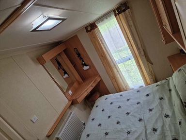 a bedroom with a bed, mirror, and curtains at Woodlands Holiday Park - Holiday Accommodation 21859, Twywn