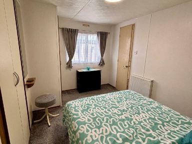 a bedroom with a bed, a window, a cabinet, and a radiator at Valley Farm Holiday Park - Holiday Accommodation 22153, Clacton-on-Sea