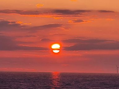 a sunset over the ocean with clouds and a wind turbine in the distance at Ty Gwyn Caravan Park - Holiday Accommodation 22189, Abergele