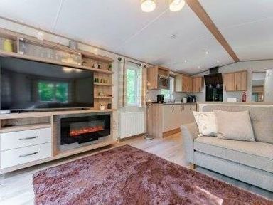a living room with a large TV, fireplace, and kitchen area at Kelling Heath Holiday Park - Holiday Accommodation 22244, Holt