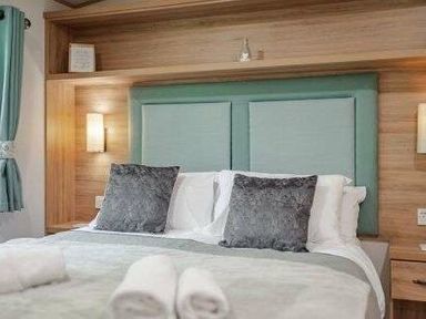 a bedroom with a double bed, decorative pillows, and wooden shelving at Kelling Heath Holiday Park - Holiday Accommodation 22244, Holt