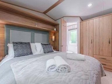 a bedroom with a central bed, two pillows, and towels on a quilt at Kelling Heath Holiday Park - Holiday Accommodation 22244, Holt