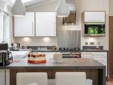 a modern kitchen with white cabinets, a stainless steel sink, and pendant lights at Kelling Heath Holiday Park - Holiday Accommodation 22249 in Holt