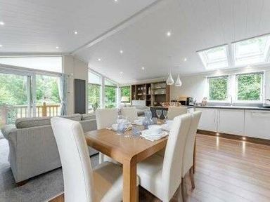 a dining area with a wooden table set for a meal and a modern kitchen at Kelling Heath Holiday Park - Holiday Accommodation 22249, Holt
