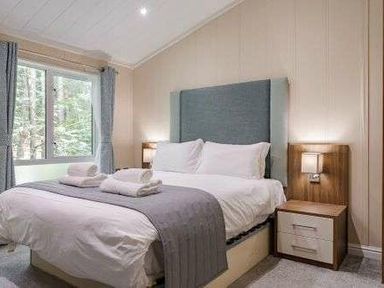 a bedroom with a bed, bedside tables, and windows at Kelling Heath Holiday Park - Holiday Accommodation 22249, Holt