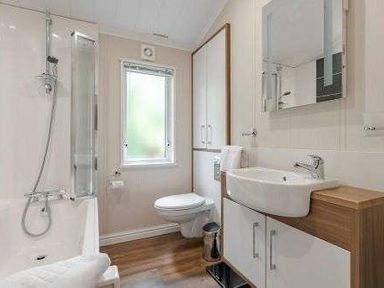 a bathroom featuring a bathtub, toilet, sink with cabinet, and a mirror at Kelling Heath Holiday Park - Holiday Accommodation 22249, Holt