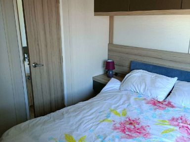 a bedroom with a bed, bedside table, lamp and a partially open door at Lyons Winkups and Primrose - Holiday Accommodation 22330 in Towyn