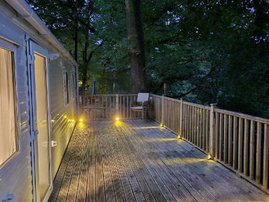 a wooden deck with lights and a chair surrounded by trees at Aberdunant Hall Holiday Park - Holiday Accommodation 22358 in Porthmadog