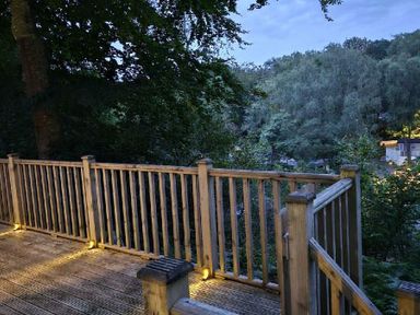 a wooden deck with a railing overlooking trees at Aberdunant Hall Holiday Park - Holiday Accommodation 22358 in Porthmadog