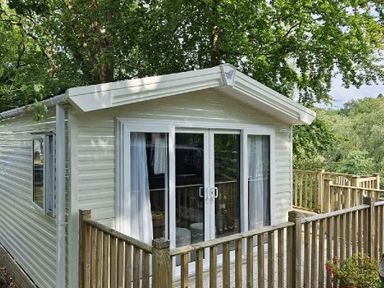 a holiday home with a wooden deck surrounded by trees at Aberdunant Hall Holiday Park - Holiday Accommodation 22358 in Porthmadog