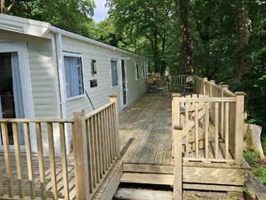 a wooden deck outside a caravan surrounded by trees at Aberdunant Hall Holiday Park - Holiday Accommodation 22358 in Porthmadog