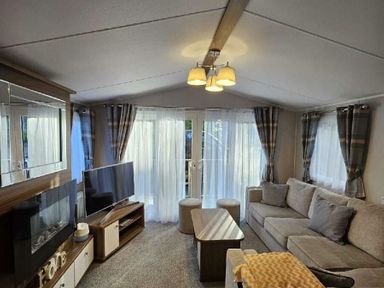 a living room with a sofa, coffee table, television, and large windows at Aberdunant Hall Holiday Park - Holiday Accommodation 22358 in Porthmadog