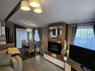 a living room with a sofa, dining table, and TV at Aberdunant Hall Holiday Park - Holiday Accommodation 22358 in Porthmadog