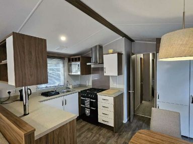 a kitchen with cabinets, a stove, and a dining area at Aberdunant Hall Holiday Park - Holiday Accommodation 22358, Porthmadog