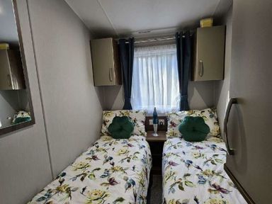 a bedroom with two beds, floral bedding, a nightstand, and curtains at Aberdunant Hall Holiday Park - Holiday Accommodation 22358, Porthmadog