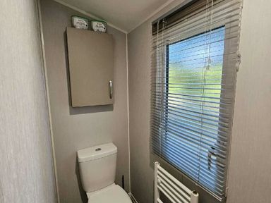 a bathroom with a toilet and a window with blinds at Aberdunant Hall Holiday Park - Holiday Accommodation 22358, Porthmadog