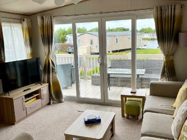 a living room with a TV and sliding glass doors leading to a deck at Lakeland Leisure Park - Holiday Accommodation 3166 Flookburgh