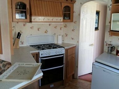 a kitchen with wooden cabinets and a gas stove at Edwards Leisure Park - Holiday Accommodation 318, Towyn