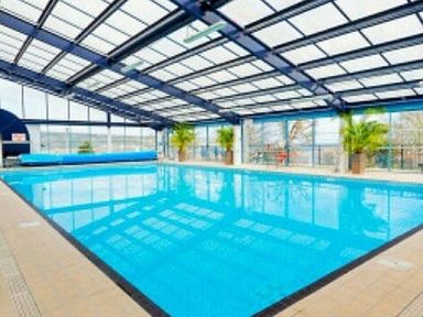 an indoor swimming pool with glass roof and blue water at Swanage Bay View - Holiday Accommodation 464 in Swanage