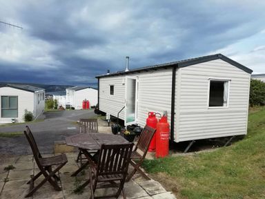 a caravan parked on a grassy area with two red gas cylinders and a wooden table with chairs at Swanage Bay View - Holiday Accommodation 464 in Swanage