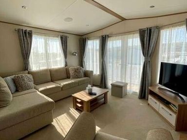 a living room with large windows, a sofa, a coffee table and a TV at Greenacres Holiday Park - Holiday Accommodation 6757 in Porthmadog