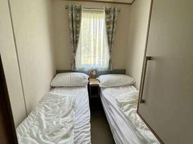 a small bedroom with two single beds and a window with curtains at Greenacres Holiday Park - Holiday Accommodation 6757 in Porthmadog