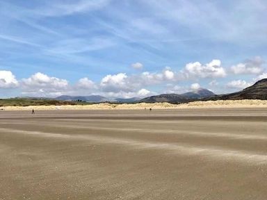 a sandy beach with distant mountains and blue sky at Greenacres Holiday Park - Holiday Accommodation 6757 Porthmadog