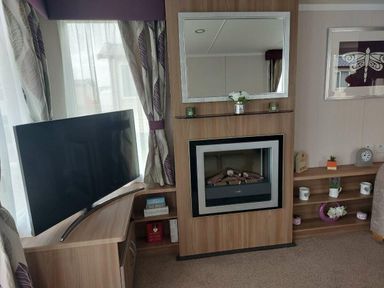 a living room with a TV, electric fireplace, and shelving at Reighton Sands Holiday Park - Holiday Accommodation 6837, Filey