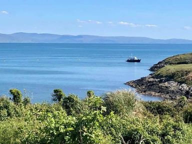 a boat on calm water near a rocky shore with greenery at Hafan y Mor Haven - Holiday Accommodation 7421 Pwllheli
