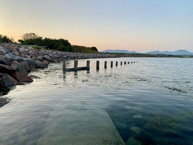 a shoreline with wooden posts in the water at Hafan y Mor Haven - Holiday Accommodation 7421 Pwllheli
