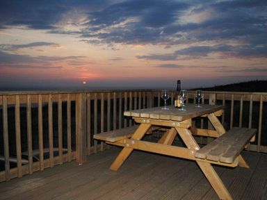 a wooden picnic table with glasses and a bottle at sunset at Perran Sands - Holiday Accommodation 7528, Perranporth, Cornwall, United Kingdom