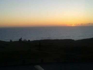 a sunset over the ocean with people sitting on the shore at Perran Sands - Holiday Accommodation 8131 Perranporth