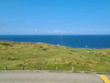 a grassy area near the ocean with a person paragliding at Perran Sands - Holiday Accommodation 8131 Perranporth